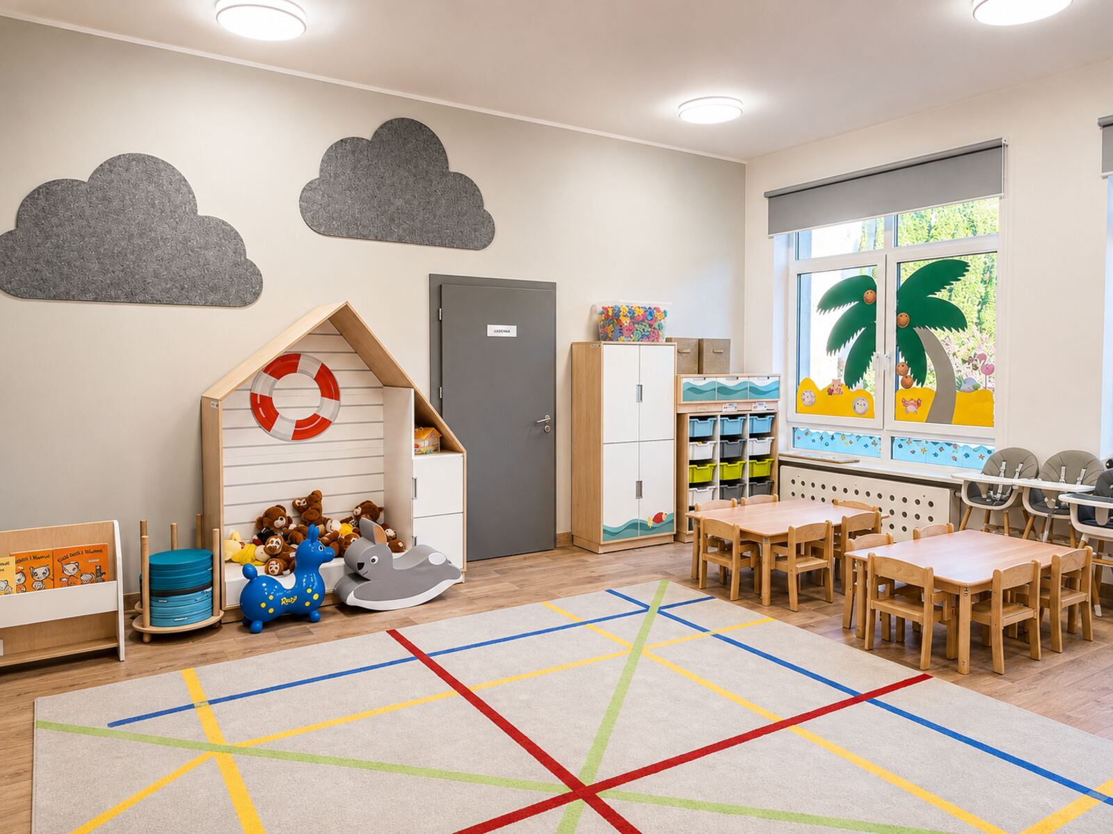 Sala zabaw z drewnianym domkiem, stolikami i kolorowym dywanem