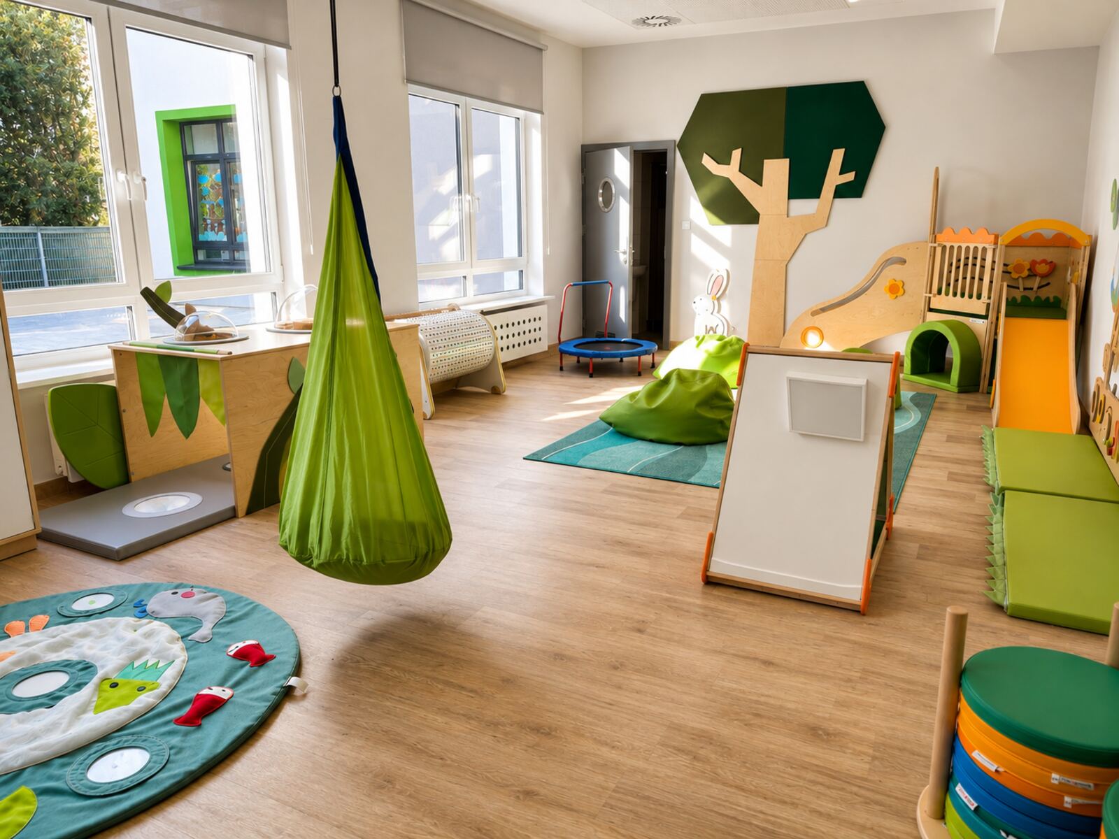 Sala sensoryczna z zieloną huśtawką-kokonem i miękkimi matami